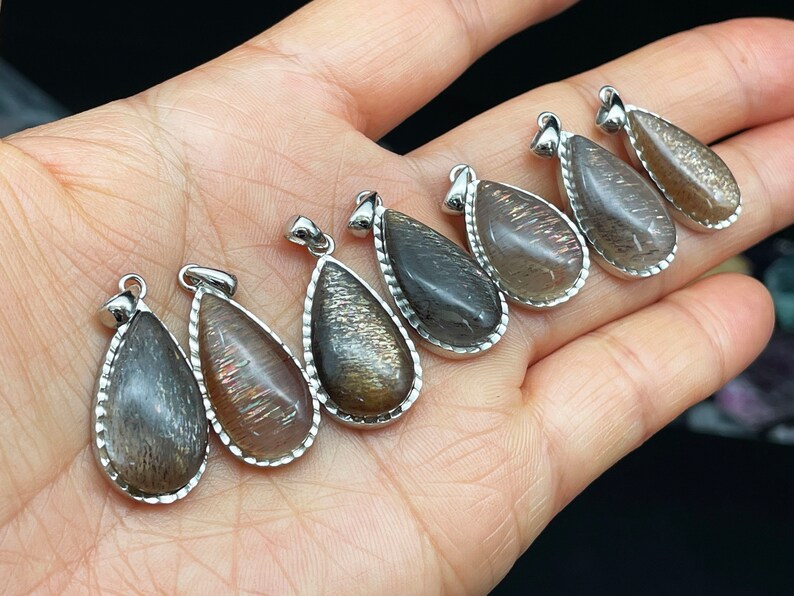 May include: Seven teardrop-shaped pendants with a silver-toned metal setting. The pendants are made of a dark, iridescent stone with a shimmery, metallic finish.