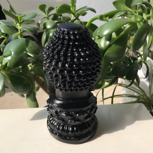 Puede incluir: Estatua de Buda negra con una cabeza detallada y una base de loto. La estatua est&aacute; hecha de un material negro liso.