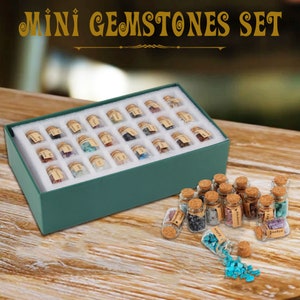 Puede incluir: Un conjunto de 24 pequeños frascos de vidrio llenos de piedras preciosas de varios colores. Los frascos están dispuestos en una caja verde con acolchado de espuma blanca. Los frascos tienen tapas de corcho y están etiquetados con el tipo de piedra preciosa.