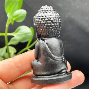 May include: A small black obsidian Buddha statue in a seated meditation pose. The statue has a detailed head and face, and is sitting on a small base.