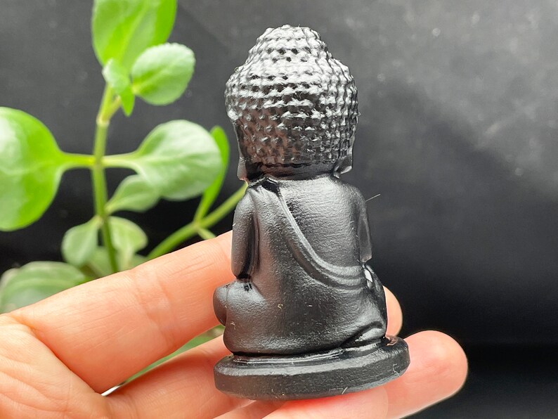 May include: A small black obsidian Buddha statue in a seated meditation pose. The statue has a detailed head and face, and is sitting on a small base.