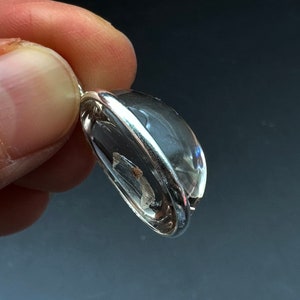 May include: A clear quartz crystal pendant with a silver setting. The crystal is oval shaped and has a slight shimmer.