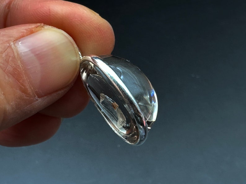 May include: A clear quartz crystal pendant with a silver setting. The crystal is oval shaped and has a slight shimmer.