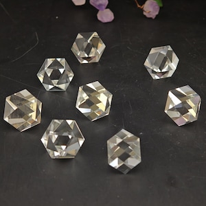 May include: Eight clear, faceted crystal gemstones in a hexagonal shape are arranged on a dark surface. The crystals have multiple reflective surfaces, catching the light and creating a sparkling effect. The gemstones are likely used for jewelry or decorative purposes.