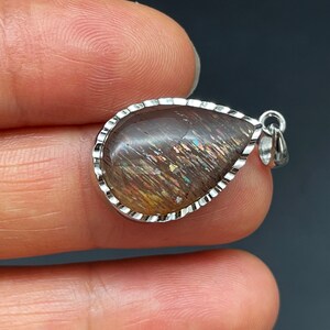 May include: A teardrop-shaped pendant with a silver setting and a brown sunstone gemstone. The gemstone has a shimmering, iridescent effect.