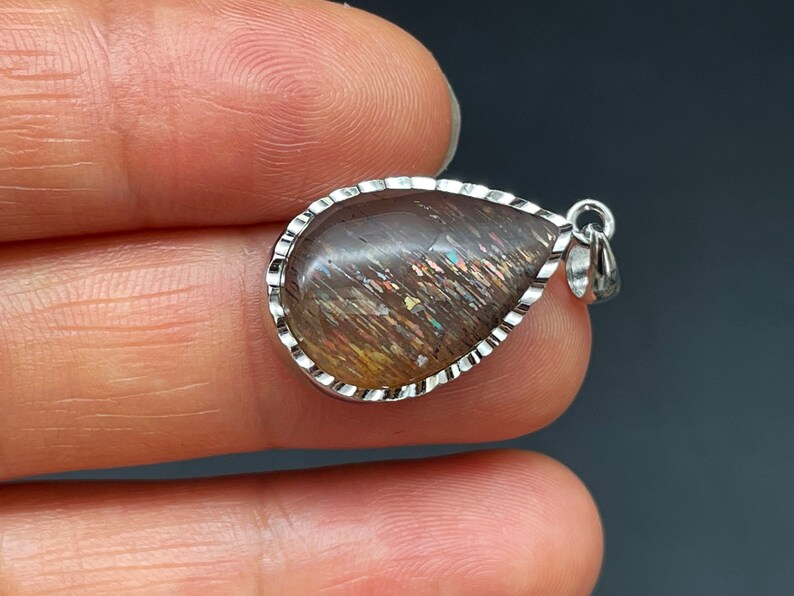 May include: A teardrop-shaped pendant with a silver setting and a brown sunstone gemstone. The gemstone has a shimmering, iridescent effect.