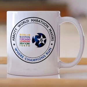 May include: White ceramic mug featuring the text "ABBOTT WORLD MARATHON MAJORS" in a circular design. The mug includes the names of marathon locations: Berlin, Boston, Chicago, London, New York, and Tokyo. A blue and white graphic with the number 6 is also featured.