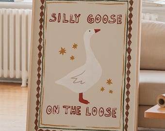 May include: A framed art print featuring a white goose illustration with red feet and beak, surrounded by stars and the text "Silly Goose On The Loose." The artwork has a beige background and a brown border.