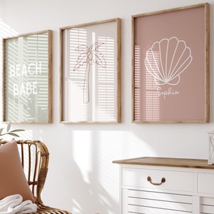 May include: A white cabinet with two drawers and two doors, a wicker chair with a brown cushion and a white throw blanket, a woven basket, and three framed prints on the wall. The prints feature a palm tree, a seashell, and the text "Beach Babe".