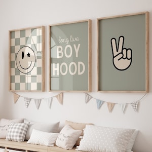 Könnte beinhalten: Drei gerahmte Drucke an einer weißen Wand über einer Holzbank mit Aufbewahrungskisten. Die Drucke zeigen einen karierten Hintergrund mit einem Smiley, den Text "long live boyhood" und ein Peace-Zeichen.