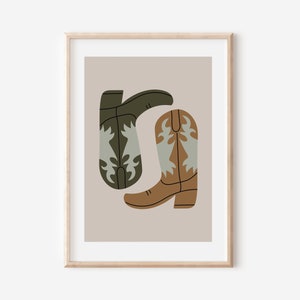 May include: A framed print of a minimalist illustration of two cowboy boots. One boot is brown with a light blue design and the other is green with a light blue design. The boots are on a light brown background.