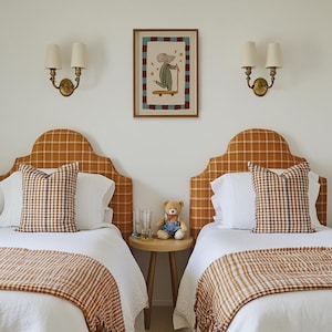 May include: Two single beds with orange check headboards and matching throws. Each bed has a white pillow and a check cushion. A small wooden table between the beds holds a teddy bear, two glasses, and a framed picture of a mouse on a skateboard.