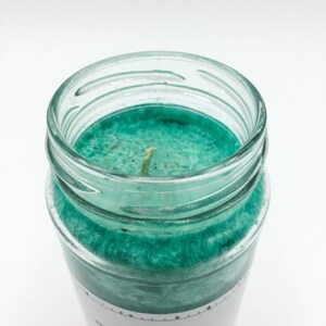 May include: A teal green candle in a glass jar with a white label that reads "Attracts luck, chance, forget, comfort, financial abundance, you can reverse the flow of events, opens a door to a new beginning".