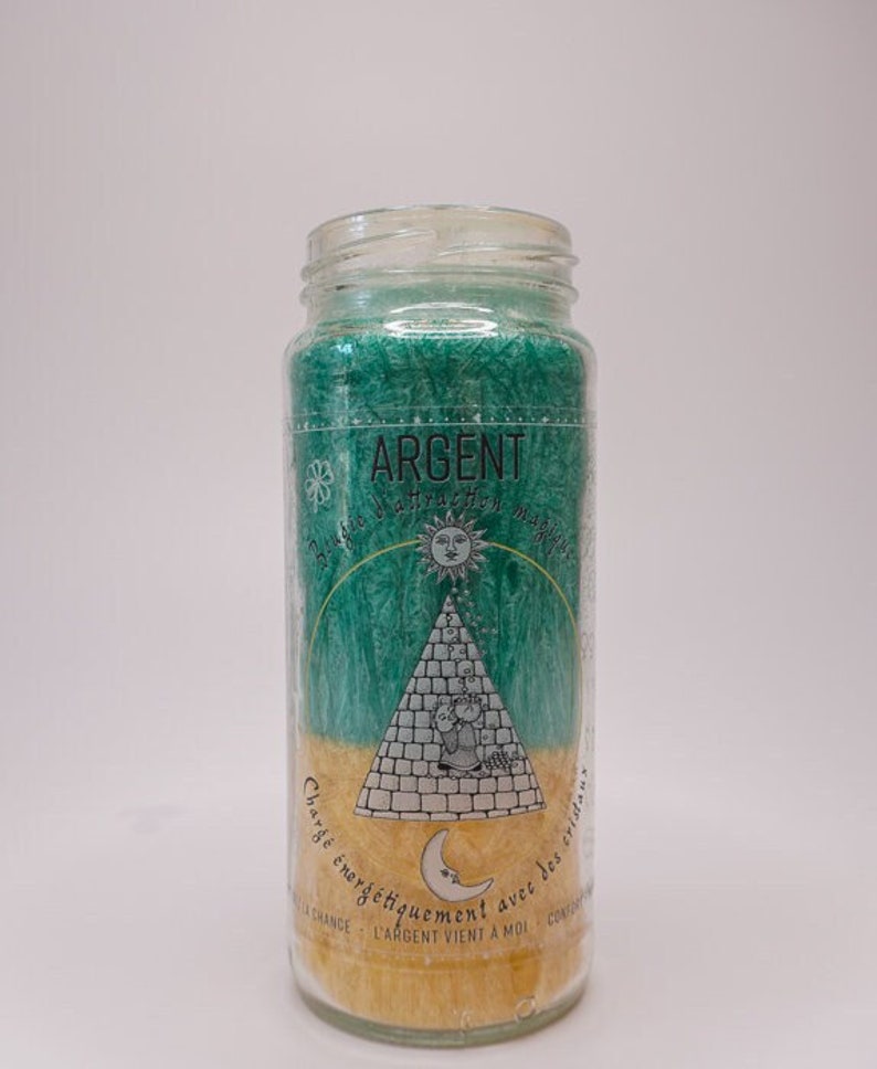 May include: A green and yellow glass candle with the word "ARGENT" printed on the label. The candle has a sun, moon, and pyramid design. The text on the label reads "Charg&eacute; &eacute;nerg&eacute;tiquement avec des vibrations... L'argent vient &agrave; moi."
