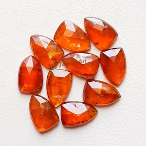 May include: A selection of faceted, orange-red gemstones. The gems are various shapes, some elongated, others more rounded. The facets reflect light, creating a sparkling effect. The text "My Jewels Art" is visible on the image.