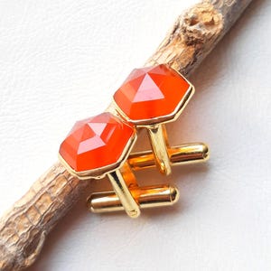 Puede incluir: Un par de gemelos de oro con piedras preciosas de cornalina naranja. Los gemelos son de forma hexagonal y tienen un acabado pulido.