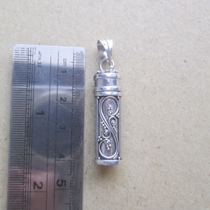 Pode incluir: Pingente de prata com forma cilíndrica e um design floral intrincado. O pingente mede aproximadamente 5 cm de comprimento e tem uma tampa com dobradiça.