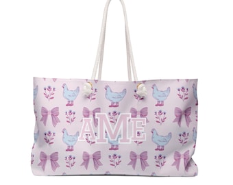 May include: A large tote bag with a pale pink background featuring a repeating pattern of blue chickens wearing boots, pink bows, and floral accents. The letters "AME" are in the centre in pink.