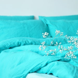 May include: A turquoise linen duvet cover and pillowcases with a sprig of white baby's breath flowers on top. The bedding is soft and luxurious, perfect for a restful night's sleep.