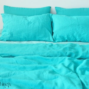 Może przedstawiać: Turkusowa poszwa na kołdrę i poszewki na poduszki z lnu. Pościel jest ułożona na łóżku z białą głową.