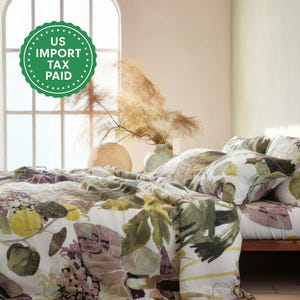May include: A bed with a floral patterned duvet cover and matching pillows. The design features green, yellow, and purple leaves on a white background. The bed is on a wooden frame, and a green circle with the text "US IMPORT TAX PAID" is visible.