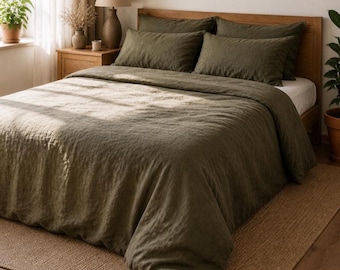 May include: An olive green linen bedding set on a wooden bed frame. The set includes a duvet cover and pillowcases. The bed is placed on a natural fiber rug. A lamp and potted plants are visible in the background, creating a cozy bedroom setting.