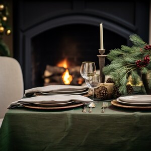 Pode incluir: Uma toalha de mesa verde com uma mesa posta para um jantar festivo. A mesa est&aacute; posta com dois pratos, guardanapos, talheres e copos de vinho. H&aacute; uma lareira no fundo com fogo a arder. Um ramo de pinho com bagas vermelhas est&aacute; no centro da mesa.