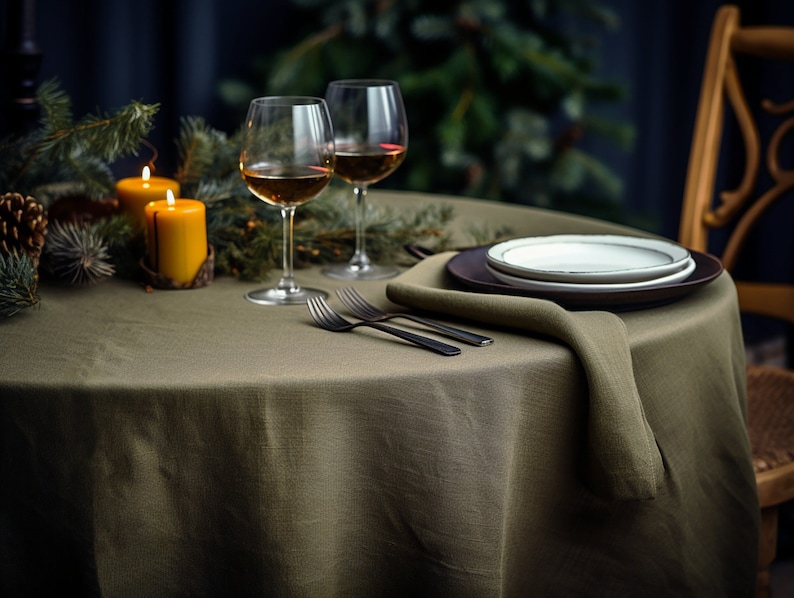 Pode incluir: Uma toalha de mesa de linho verde com um prato castanho, um prato branco e um guardanapo. Duas ta&ccedil;as de vinho e duas velas acesas est&atilde;o sobre a mesa.