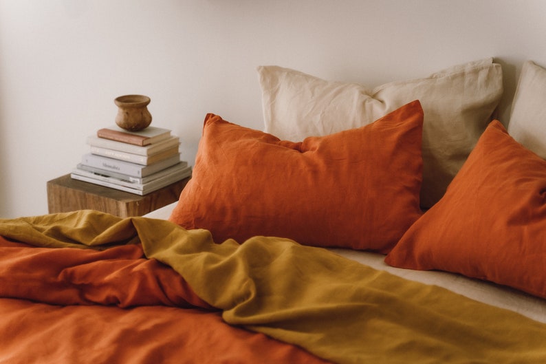 May include: A bed with a rust-colored duvet cover and a mustard yellow throw blanket. There are three pillows on the bed, two are rust-colored and one is cream-colored.