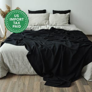 May include: A bed with a light gray duvet cover and pillows, topped with a black blanket. The pillows are white and black. The image includes a green circle with the text "US IMPORT TAX PAID".