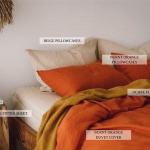 May include: A bed with a burnt orange duvet cover and ochre flat sheet. The bed has beige fitted sheet and two beige pillowcases. There are two burnt orange pillowcases on top of the beige pillowcases.