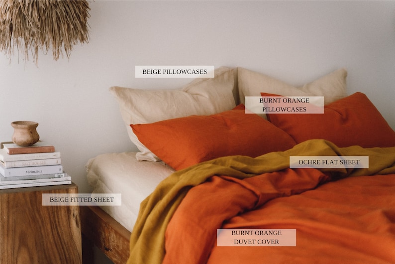 May include: A bed with a burnt orange duvet cover and ochre flat sheet. The bed has beige fitted sheet and two beige pillowcases. There are two burnt orange pillowcases on top of the beige pillowcases.