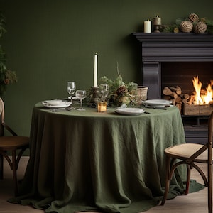 Pode incluir: Uma mesa de jantar r&uacute;stica com uma toalha de mesa de linho verde, cadeiras de madeira e uma lareira no fundo. A mesa est&aacute; posta com pratos, copos e velas.