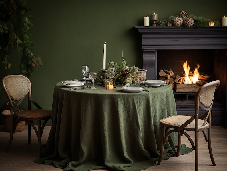Pode incluir: Uma mesa de jantar r&uacute;stica com uma toalha de mesa de linho verde, cadeiras de madeira e uma lareira no fundo. A mesa est&aacute; posta com pratos, copos e velas.