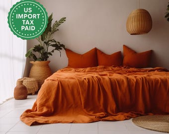 Può includere: Una scena di camera da letto con un copriletto di lino arancione e federe abbinate. Una lampada a sospensione intrecciata è appesa sopra il letto. Piante decorative in cesti intrecciati e un tappeto rotondo intrecciato completano l'estetica calda e invitante.