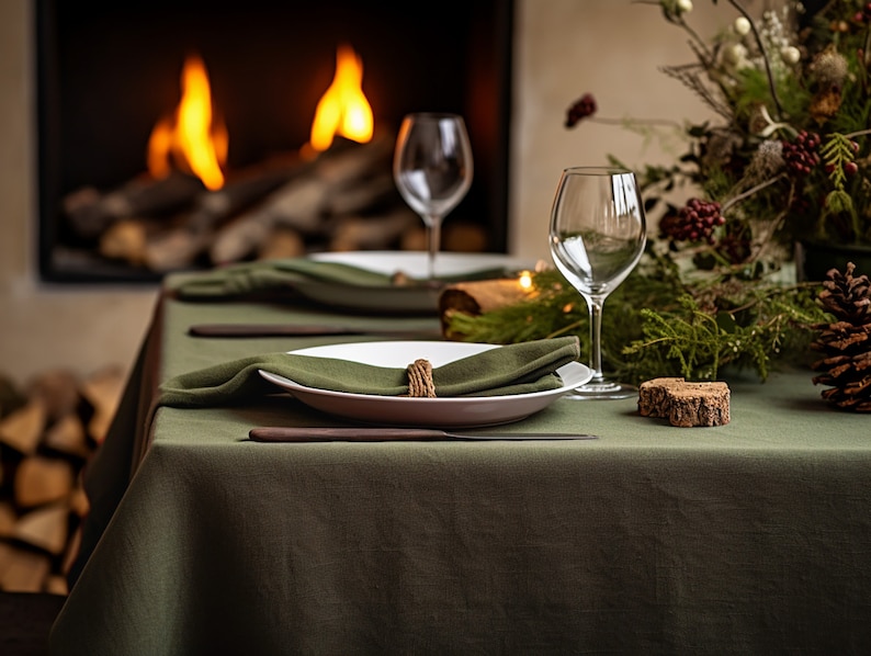 Pode incluir: Uma toalha de mesa de linho verde preparada para um jantar com pratos brancos, guardanapos verdes e um descanso de copo de madeira. A mesa est&aacute; posta em frente a uma lareira com fogo.