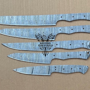 Peut inclure: Cinq lames de couteau sans manche de tailles variées, présentant chacune un motif ondulé gris et argenté distinct sur la surface métallique. Les lames ont des trous pré-percés dans la soie et un logo central KESTREL INDUSTRIES.