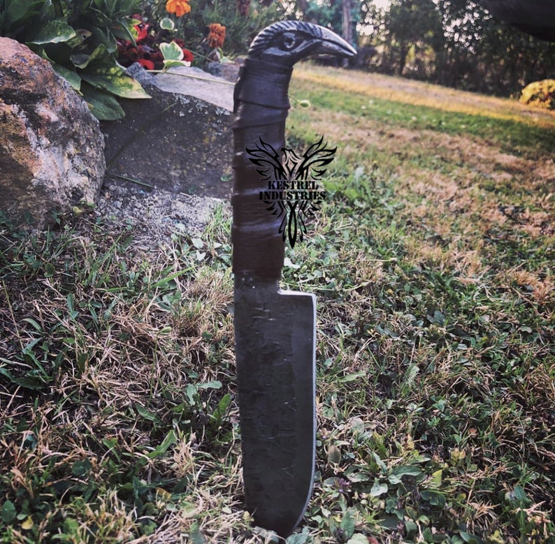 Pu&ograve; includere: Un coltello nero con un manico a forma di uccello. Il manico &egrave; avvolto in pelle marrone e la lama &egrave; in metallo. Il coltello &egrave; in piedi su un letto di erba verde.
