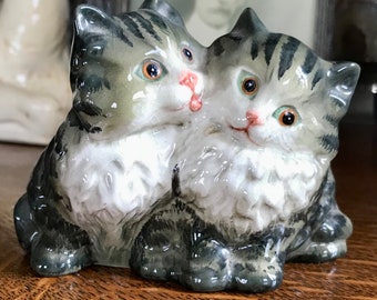 May include: A porcelain figurine of two gray and white kittens cuddling. The kittens have black stripes and realistic details, including painted eyes and whiskers.