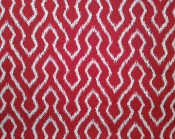 May include: Red fabric with a white ikat pattern. The design features a repeating geometric motif of diamond shapes connected by vertical lines, creating a textured visual effect. This textile is suitable for home decor.