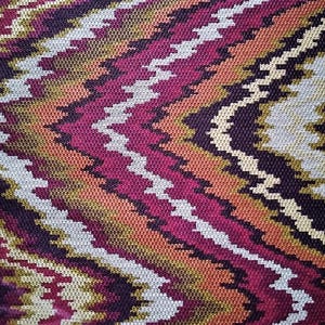May include: A close-up of a fabric with a zig-zag pattern in shades of red, orange, brown, white, and black.