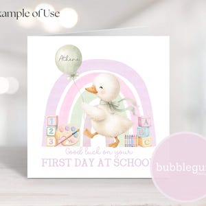Puede incluir: Tarjeta de felicitación cuadrada con una ilustración en acuarela de un pato sosteniendo un globo con el nombre "Athena". La tarjeta incluye un arcoíris pastel, bloques y el texto "Good luck on your FIRST DAY AT SCHOOL".