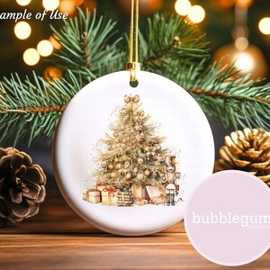 May include: A white ceramic Christmas ornament with a watercolor illustration of a gold Christmas tree with presents and a nutcracker. The ornament is hanging from a gold string.