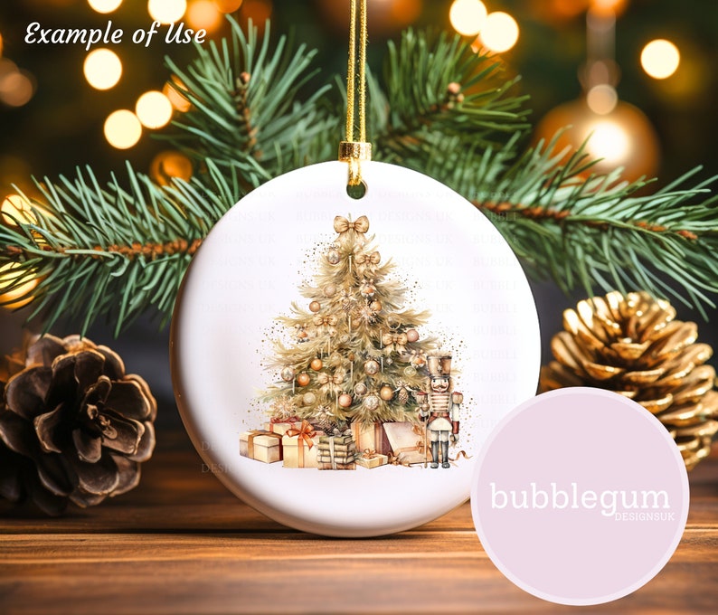 May include: A white ceramic Christmas ornament with a watercolor illustration of a gold Christmas tree with presents and a nutcracker. The ornament is hanging from a gold string.