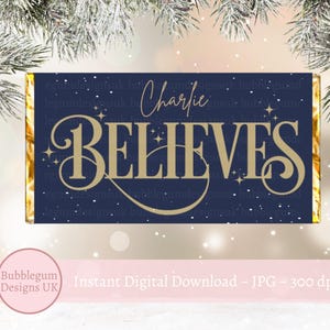 Op de afbeelding: Een downloadbare digitale print van een blauwe en gouden kerstchocolade-wikkel met de tekst "Charlie Believes" in een gouden handschrift.