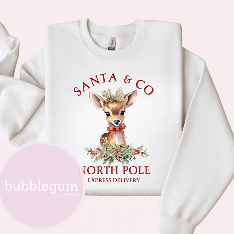 K&ouml;nnte beinhalten: Wei&szlig;er Pullover mit einem roten und gr&uuml;nen Weihnachtsmotiv. Das Motiv zeigt ein s&uuml;&szlig;es Cartoon-Reh mit einer roten Schleife und dem Text "Santa & Co. North Pole Express Delivery".
