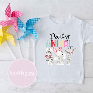 May include: White t-shirt with a colorful "Party Animal" graphic featuring a zebra, elephant, and giraffe wearing sunglasses. The graphic is surrounded by a rainbow of colors.