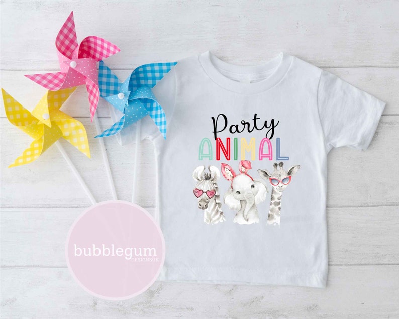 May include: White t-shirt with a colorful "Party Animal" graphic featuring a zebra, elephant, and giraffe wearing sunglasses. The graphic is surrounded by a rainbow of colors.