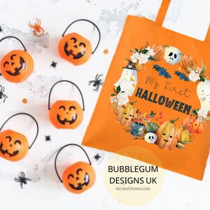 Pode incluir: Sacola de tecido laranja e branca com o texto "My First Halloween" e uma ilustra&ccedil;&atilde;o em aquarela de ab&oacute;boras, fantasmas e morcegos. A sacola tem um fundo branco e o texto est&aacute; em preto.