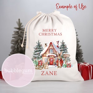 May include: White canvas Christmas gift bag with a red and white illustration of a snow-covered house, a bunny, and a sleigh. The bag has the text "Merry Christmas" and "Zane" printed on it.